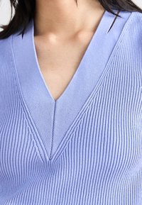 Maglione a coste di un leggero viola con scollo a V, caratterizzato da dettagli di cucitura sottili e una finitura testurizzata.