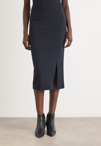 Knee-length navy pencil skirt with a side slit, made from stretchy fabric. Paired with black pointed ankle boots. Smooth texture.