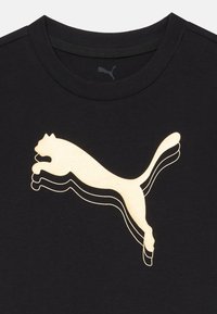 Svart bomulls-T-skjorte med en stor gull Puma-logo i en hoppende posisjon, med lagde konturer som skaper dybde og en jevn tekstur.