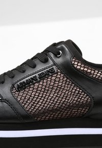 Baskets noires avec côtés en mesh, lacets noirs et marquage "Armani Jeans" sur la tige en cuir près des lacets.