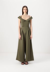 Olivengrønn jumpsuit med avtagbare skulderstropper, plisserte vide ben og en tettsittende overdel. Laget av glatt, strukturert stoff.