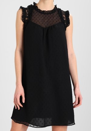 Robe noire avec une texture à pois, dotée d'un col en tulle froncé et d'accents sur les épaules. Longueur au-dessus du genou et coupe ample.