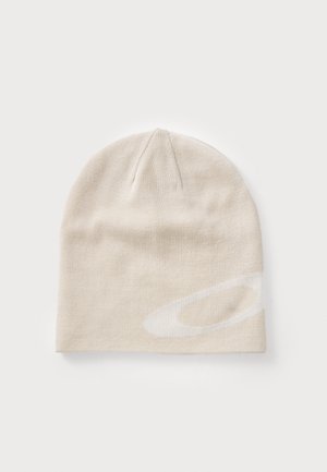 Vaaleanbeige neulottu pipo, jossa on pyöreä yläosa ja hillitty, suuri valkoinen logo. Pehmeä materiaali ja joustava istuvuus tarjoavat mukavuutta.