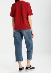 Camiseta roja de manga corta combinada con unos jeans cortos de tiro alto y holgados de color azul claro, con dobladillos deshilachados y zapatillas negras.