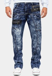 Jeans in denim di un blu scuro con aree sbiadite, molteplici tasche, un compartimento con zip e un accento nero testurizzato sulla vita.