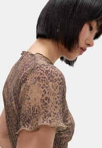 Brun genomskinlig topp med leopardmönster, med veckade kanter och ett strukturerat tyg, designad med en rundad halsringning.