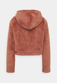 Chaqueta corta con capucha de suave y esponjoso forro polar de color óxido. Presenta mangas largas con puños ajustados y una capucha redondeada en la parte posterior.