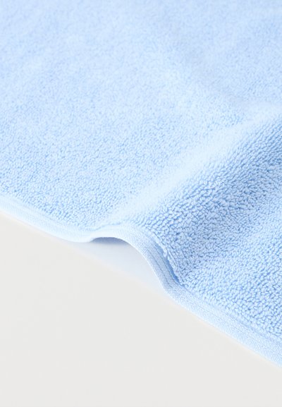 Μαλακή πετσέτα μικροϊνών σε ανοιχτό μπλε χρώμα με υφή, διπλωμένη σε λευκό φόντο.