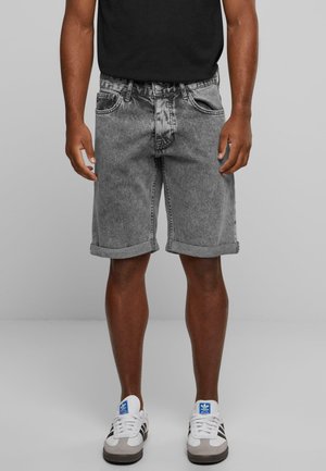 Graue Denim-Shorts mit umgeschlagenem Saum und Fünf-Taschen-Design, kombiniert mit einem schwarzen Shirt und weißen Sneakers mit blauen Akzenten.