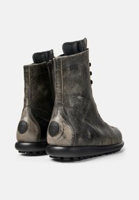 Bottines noires en cuir avec une finition usée, fermeture éclair sur le côté, panneaux texturés et semelles en caoutchouc moulé présentant des motifs de semelles circulaires.