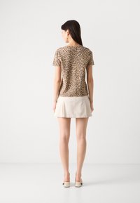 Korte erm leopardmønstret topp i beige og brunt, sammen med en lys beige skorts. Glatt stoff med en avslappet passform.