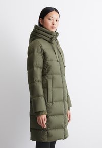 Puffjack in olijfgroen, met een hoge kraag, ritssluiting en geribde manchetten. Gevoerde ontwerpen met zijzakken en een gladde textuur.