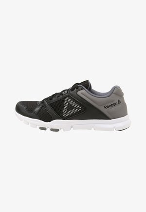 Zapatilla deportiva Reebok negra y gris con suela blanca, paneles de malla y logo en el lateral sobre fondo blanco.