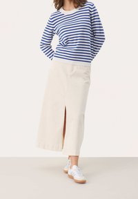 Sweter w niebiesko-białe paski, kremowa długa spódnica z przednim rozcięciem, zestawione z białymi trampkami z gumowymi podeszwami. Gładkie tekstury tkanin.