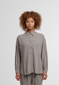 Gray long-sleeve button-up shirt made from soft fabric, featuring a collar, front buttons, and a relaxed fit. Slightly curved hemline.