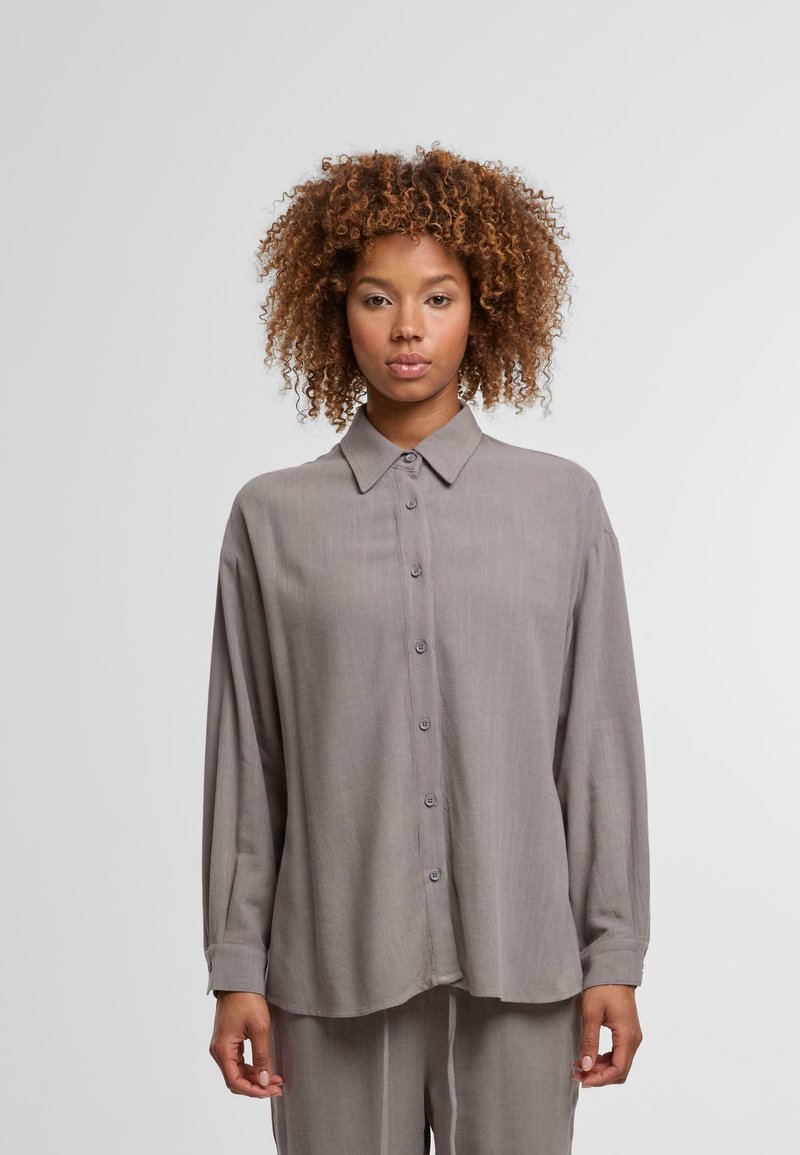 Gray long-sleeve button-up shirt made from soft fabric, featuring a collar, front buttons, and a relaxed fit. Slightly curved hemline.
