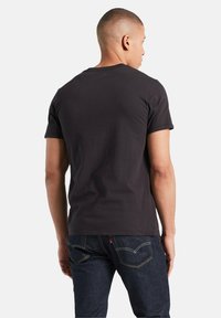 Sort kortærmet t-shirt lavet af bomuld, med rund hals og en glat tekstur, parret med mørke denimjeans synlige ved taljen.