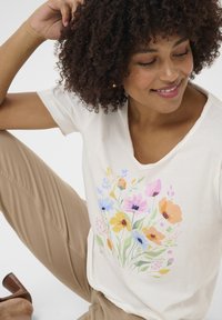 Light cream t-shirt featuring a colorful floral print with shades of pink, blue, yellow, and green. Soft texture, relaxed fit, and short sleeves.