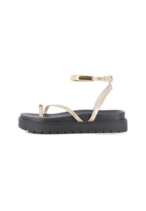 Sandalia de plataforma negra con tiras finas beige, incluyendo una sujeción para el dedo y una hebilla en el tobillo con detalle metálico.