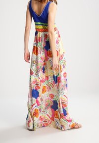 Robe maxi avec un haut bleu et une jupe à motifs floraux colorés. Elle présente une taille cintrée et un tissu fluide. Comprend un design dos en V.