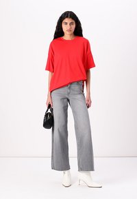 Red oversized t-shirt, short sleeves, paired with light gray wide-leg jeans. Model holds a black handbag and wears white pointed boots.