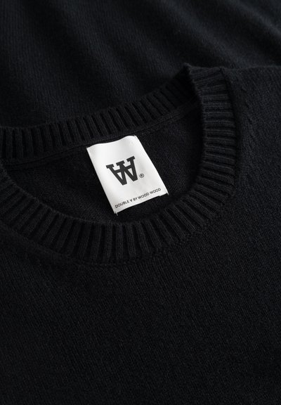 Suéter negro de punto con cuello acanalado, que presenta una etiqueta de marca blanca con el texto "DOUBLE Y BY WOOD WOOD". Textura suave, diseño minimalista.