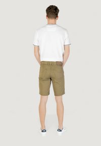 Shorts leggeri di colore verde oliva con taglio dritto, passanti per cintura, due tasche posteriori e una texture del tessuto liscia. Abbinati a una camicia bianca a maniche corte.