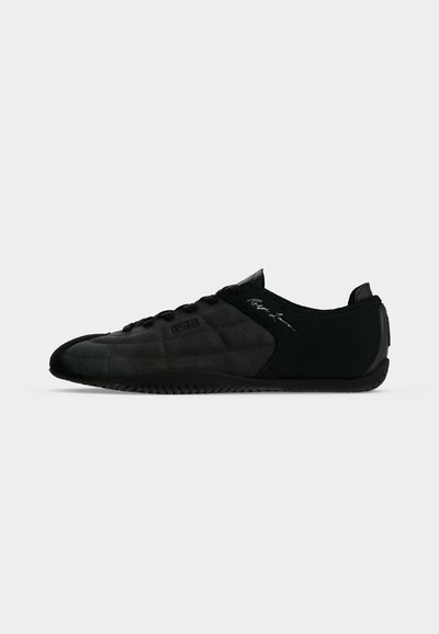 Μαύρο sneaker χαμηλού προφίλ με επάνω μέρος από σουέντ και ύφασμα, υφή στη σόλα, κλείσιμο με κορδόνια και λεπτή λεπτομέρεια υπογραφής στο πλάι.