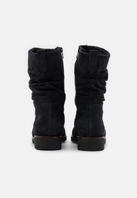 Svarta mocka anklar stövlar med en slouchy design, bakre dragkedjor och texturerade gummisulor. Fleece-foder synligt vid den övre öppningen.