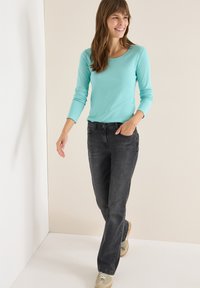 Jasnoniebieska bluzka z długim rękawem zestawiona z ciemnoszarymi dżinsami. Modelka ma na sobie beżowe sneakersy. Stylizacja jest casualowa i wygodna w kroju.
