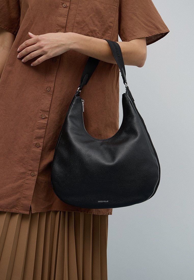 Sac hobo en cuir noir avec une texture lisse, une silhouette courbée et une sangle ajustable. Présente un logo discret à l'avant.