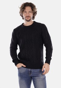 Maglione nero lavorato a maglia con motivi a trecce testurizzati, scollo a girocollo e polsini e vita a coste, abbinato a jeans blu.