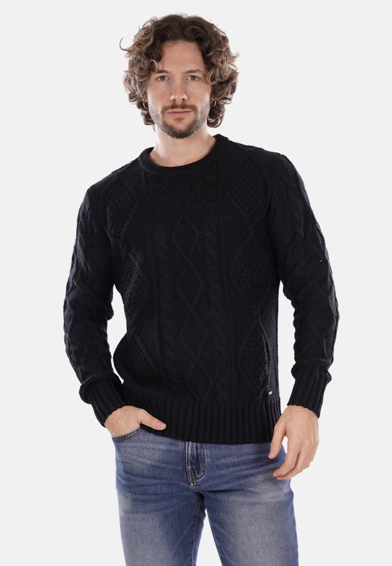 Maglione nero lavorato a maglia con motivi a trecce testurizzati, scollo a girocollo e polsini e vita a coste, abbinato a jeans blu.