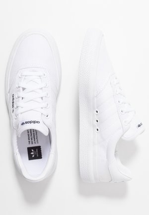 Paar weiße Adidas-Sneaker mit Schnürsenkeln, sichtbares Logo auf der Zunge und der Seite, strukturierte Sohle, gezeigt von oben und von der Seite.