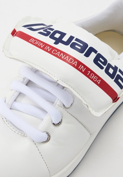 White leather sneaker with round toe, white laces, and silver eyelets; features a padded tongue with red and blue branding.