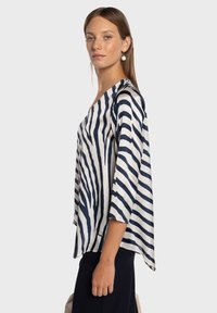 Blouse rayée bleu marine et blanche en tissu léger et lisse, avec une coupe décontractée, un décolleté en V et des manches trois-quarts.