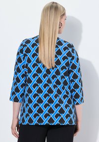 Maglia blu e nera con un motivo geometrico, maniche a 3/4 e vestibilità ampia, realizzata in tessuto leggero.
