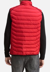 Rote Steppweste mit horizontalem Steppmuster, hohem Kragen und leichtem Material. Von hinten getragen über einem schwarzen Langarmshirt.