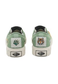 Ténis de lona verdes com sola texturada, apresentando uma pata e um bordado de tigre no calcanhar, e a marca "PALLADIUM" na parte de trás.