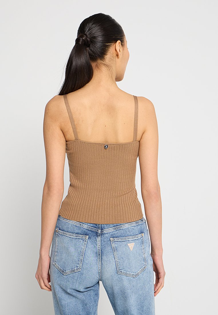 Braunes, geripptes Tanktop mit dünnen Trägern, das hinten mit einem Knopf verziert ist. Kombiniert mit hellblauen, ausgewaschenen Jeans.