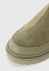 Olivengrøn suede støvle med rund tå og gummisål. Har syninger ved tåhætten og en glat overflade på sålen.