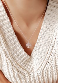 Pendente ad albero della vita in argento su una delicata catena, esposto su un maglione a maglia testurizzata di colore crema con scollatura a V.