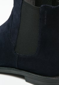 Botín Chelsea de ante navy con paneles laterales elásticos, un acabado liso en la parte superior y una suela de goma texturizada, con un diseño elegante y de altura hasta el tobillo.