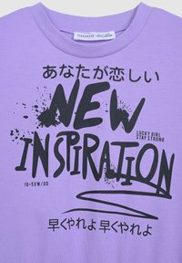 Fioletowy bawełniany T-shirt z dużym czarnym tekstem graficznym oraz akcentami w stylu splat, z napisem "NOWA INSPIRACJA" i japońskimi znakami.