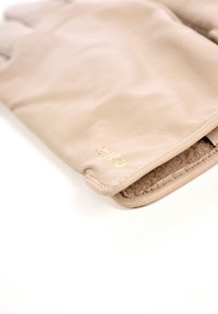 Beige læderhandsker med blottede fingerspidser. Blød tekstur, syede kanter og en lille logo trykt i guld nær manchetterne.