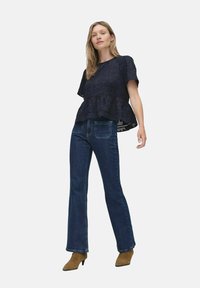 Sininen peplum-toppi, jossa on teksturoitu kangas, yhdistettynä tummansinisiin leveälahkeisiin farkkuihin. Ruskeat korkokengät korostavat asua.