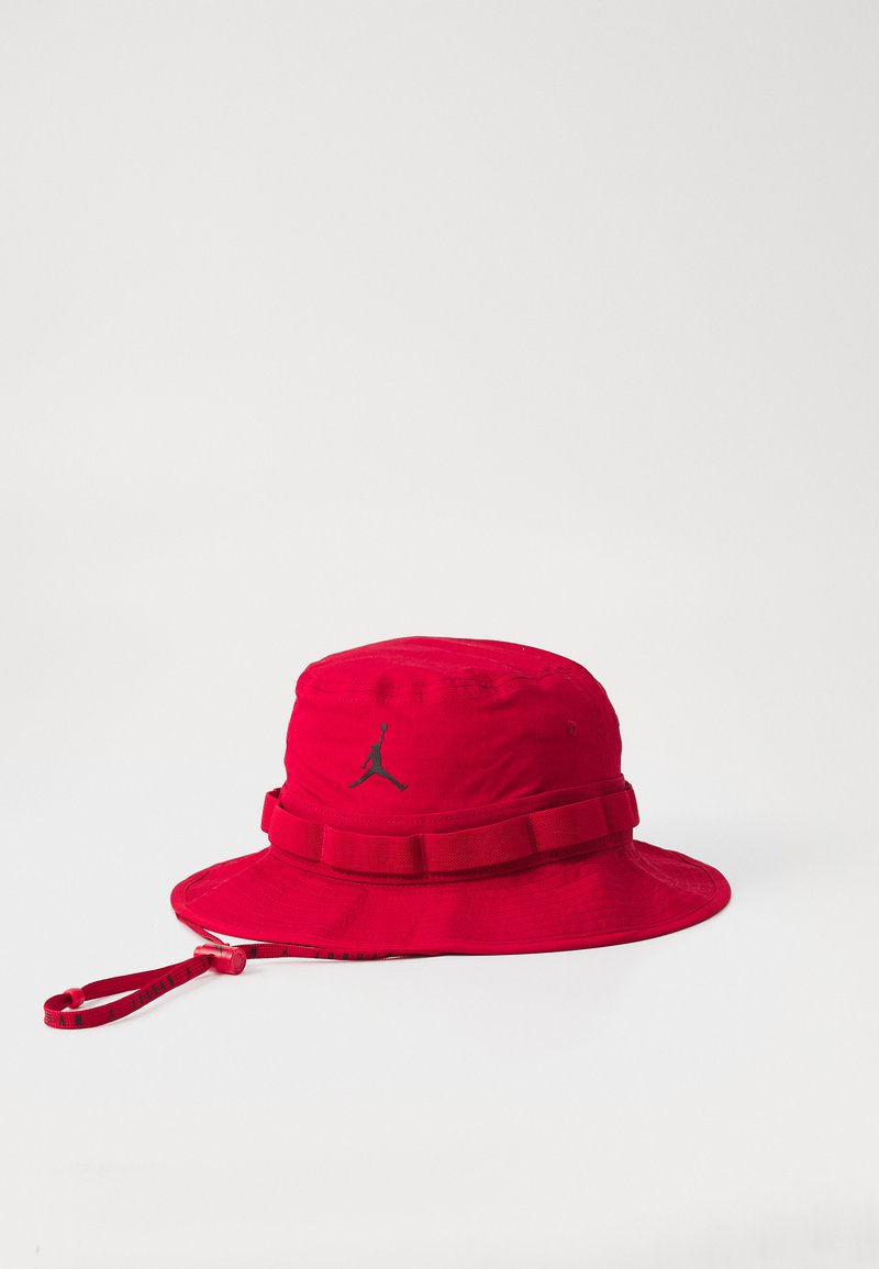 Chapeau seau rouge en nylon avec une large visière, présentant un logo Jordan noir et une sangle ajustable assortie autour de la couronne.