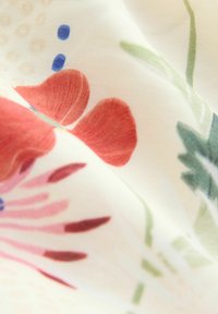 Tessuto a trama floreale in morbido bianco, caratterizzato da fiori rossi e rosa con steli verdi e accenti blu, texture liscia e design leggero.