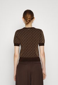 Top de punto marrón de manga corta que presenta un patrón de monograma por toda la prenda, cuello y dobladillo acanalados, con una silueta ajustada.