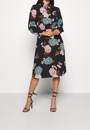 Robe noire à fleurs avec manches longues, col montant et coupe jusqu'aux genoux. Fleurs vibrantes roses et turquoise sur fond noir.